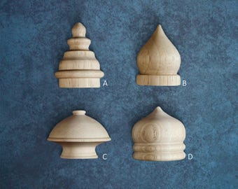 May include: Four wooden finials in various shapes, including a tiered pagoda-like design, a rounded dome, and a mushroom-shaped form. The finials are made of light-colored wood and are displayed against a textured blue background.