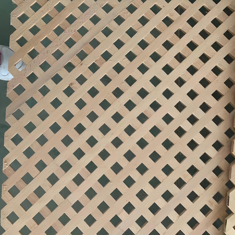 May include: Wooden lattice panel with a diamond pattern. The light brown wood is arranged in a diagonal grid, creating a series of square openings. The panel is likely for decorative or structural use.