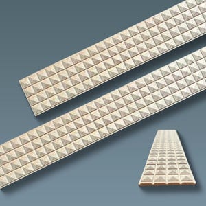 May include: Three beige decorative trim pieces with a repeating pyramid pattern. The trim is rectangular and appears to be made of wood or a similar material. The background is a solid, muted blue-grey.
