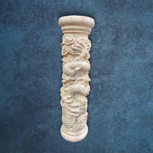 Può includere: Un pilastro beige scolpito con intricati disegni di draghi e nuvole. La colonna ha una parte superiore e inferiore arrotondate, e le sculture di draghi avvolgono il corpo del pilastro. Lo sfondo è di colore verde acqua strutturato.