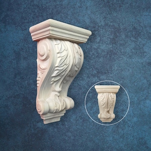May include: A light-coloured, ornate wooden corbel with a detailed scroll and leaf design. The corbel has a rectangular top and a curved, decorative body. A smaller, circular inset shows a similar corbel.