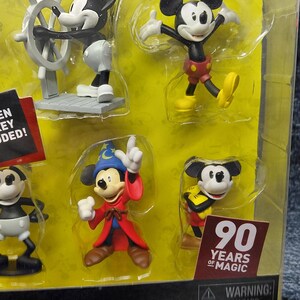 May include: A collectible deluxe figure set featuring Mickey Mouse in various poses. The set includes figures of Mickey as a captain, in a classic pose, as a sorcerer, and in a yellow and black outfit. The packaging includes the text "90 Years of Magic".