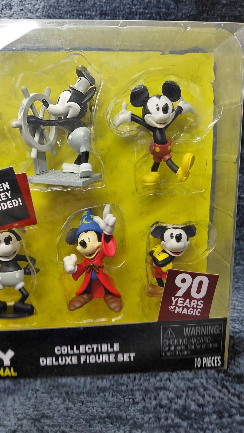 May include: A collectible deluxe figure set featuring Mickey Mouse in various poses. The set includes figures of Mickey as a captain, in a classic pose, as a sorcerer, and in a yellow and black outfit. The packaging includes the text "90 Years of Magic".