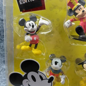 May include: A Special Edition set of Mickey Mouse figurines in a clear plastic package. The figurines depict Mickey Mouse in various poses and outfits, including a marching band uniform. The packaging includes the text "SPECIAL EDITION".