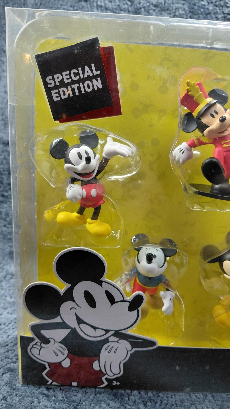 May include: A Special Edition set of Mickey Mouse figurines in a clear plastic package. The figurines depict Mickey Mouse in various poses and outfits, including a marching band uniform. The packaging includes the text "SPECIAL EDITION".