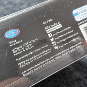 May include: Black product packaging with the Just Play logo and Disney branding. The packaging includes website addresses, social media handles, and a warning about adult supervision. Made in China.