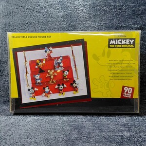 May include: Collectible Deluxe Figure Set featuring Mickey Mouse characters. The set includes various Mickey Mouse figurines in different poses, displayed on a red platform. The packaging is yellow with the text "MICKEY THE TRUE ORIGINAL" and "90 YEARS MAGIC".