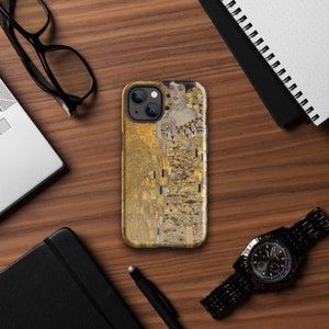 May include: A phone case featuring a gold and multi-colored artwork. The design includes a portrait of a woman with a detailed background. The case is on a wooden surface with other items, including a watch and glasses.