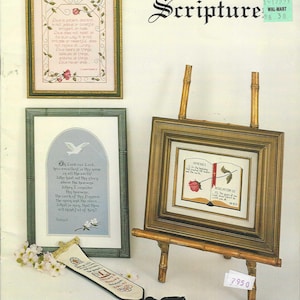 May include: An assortment of framed scripture art pieces, including a framed cross-stitch with a floral border and text. A small framed piece rests on a bamboo easel. A bookmark with a tassel is also present.