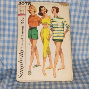 May include: Vintage Simplicity printed pattern envelope featuring three illustrations of women in retro summer outfits. The outfits include shorts, crop tops, and capri pants in orange, yellow, green, and striped tops. The envelope reads "2075" and "Size 14 Bust 34".
