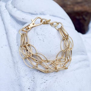 May include: A gold chain bracelet with multiple layers of oval-shaped links. The bracelet has a lobster claw clasp.