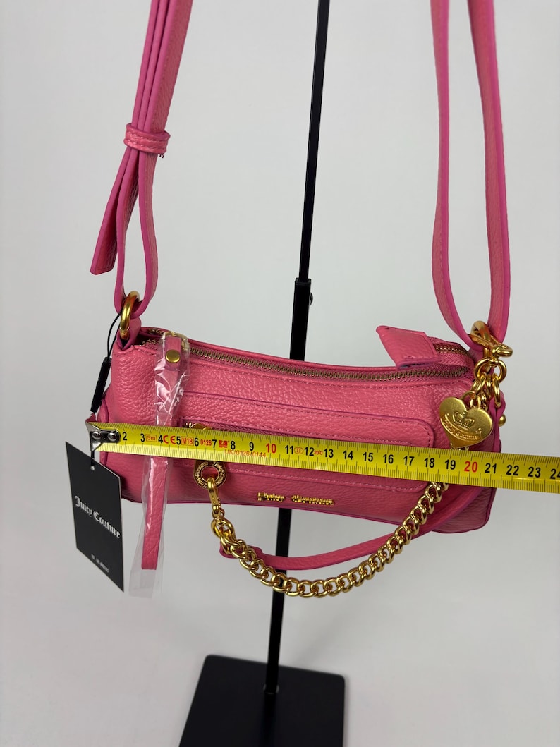 May include: A pink Juicy Couture shoulder bag with a gold chain strap and zipper. The bag is approximately 9 inches long. The bag has a gold heart charm and a tag that says Juicy Couture.