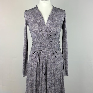 May include: A dark blue dress with a white dot pattern, long sleeves, and a V-neck. The dress has a wrap-style waist and a pleated skirt. It is displayed on a mannequin against a plain background.