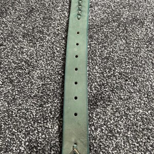 May include: A teal-colored leather belt with decorative stitching and multiple holes for adjustment. The belt has a slightly distressed appearance, suggesting it is made of genuine leather. The design includes arrow-shaped details near the buckle.