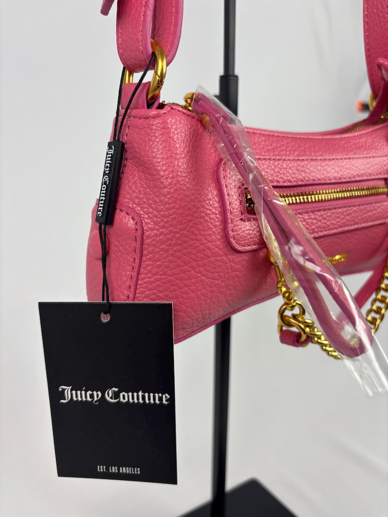 May include: A pink leather shoulder bag with gold-tone hardware, including a chain strap. The bag features a zippered closure and a small pocket on the front. A black tag with the "Juicy Couture" logo is attached.