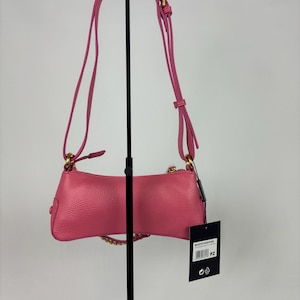 May include: A pink leather shoulder bag with a gold chain and strap. The bag is displayed on a black stand against a white background. A tag hangs from the bag.