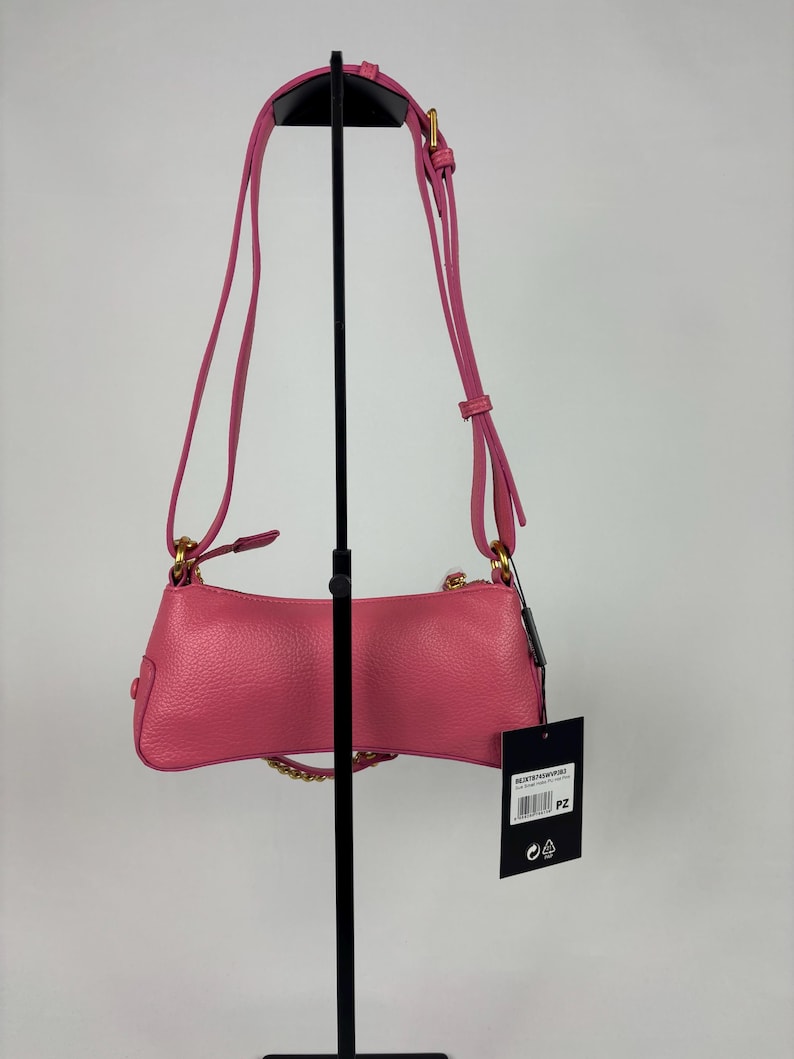May include: A pink leather shoulder bag with a gold chain and strap. The bag is displayed on a black stand against a white background. A tag hangs from the bag.