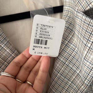 May include: A medium-sized, neutral-toned plaid blazer with a tag that reads "NEUTR MOT" and "M". The blazer is made in Vietnam. The tag also includes a price of &pound;158.00.