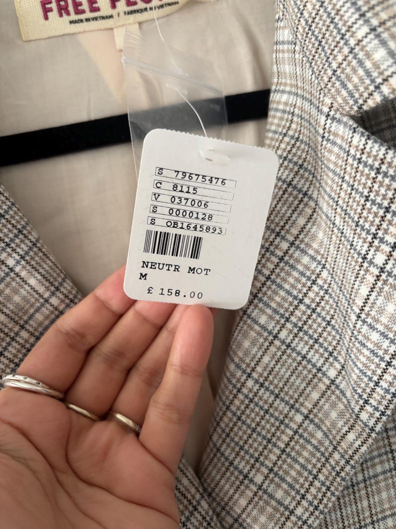 May include: A medium-sized, neutral-toned plaid blazer with a tag that reads "NEUTR MOT" and "M". The blazer is made in Vietnam. The tag also includes a price of &pound;158.00.