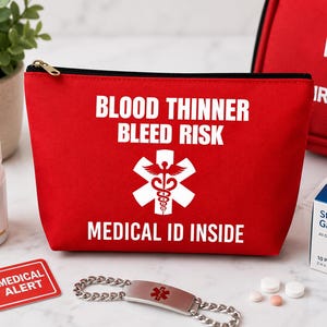 May include: A red medical pouch with the text "BLOOD THINNER BLEED RISK MEDICAL ID INSIDE" and a medical symbol. Other medical supplies include a bottle of Aspirin, a medical alert card, and a medical ID bracelet.