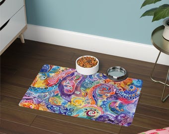 Può includere: Un tappetino rettangolare per animali domestici con un vivace motivo astratto multicolore di vortici, punti e forme simili a paisley nei toni del blu, viola, arancione e giallo, sotto una ciotola bianca con croccantini e una ciotola argentata.