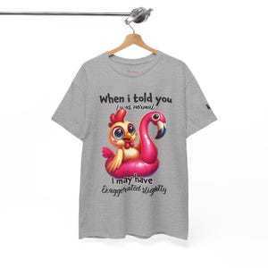 Puede incluir: Una camiseta gris con un dibujo animado de un pollo en un flotador de flamenco rosa. El texto de la camiseta dice: "Cuando te dije que era normal, puede que haya exagerado un poco."