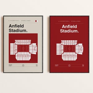 May include: Two framed prints of Anfield Stadium, Liverpool, England. The prints show a minimalist design of the stadium's layout in white against a red and beige background. Text includes "Anfield Stadium" and other details.