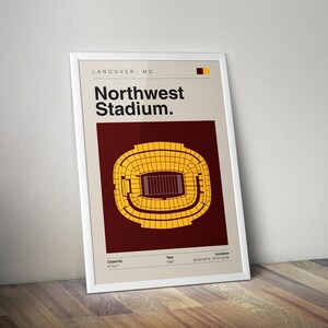 May include: A framed poster featuring a stadium schematic. The poster reads "Northwest Stadium" with the location "Landover, MD." The stadium is depicted in yellow and brown, with details on capacity, year, and location. The poster is in a white frame.