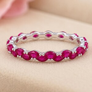 May include: A silver-toned eternity band featuring a continuous row of vibrant, marquise-cut fuchsia pink stones set in a polished metal frame. The ring showcases a repeating pattern of pointed, eye-shaped gems secured by small metal prongs.