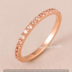 May include: A rose gold ring with a band of small, round, peach-colored gemstones. The ring is set against a soft, neutral background. The text "myasajewels" is visible on the ring.