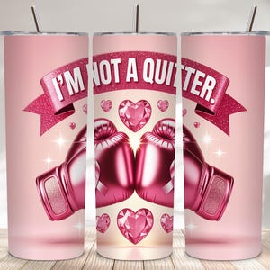 May include: A pink tumbler with a design featuring pink boxing gloves, heart-shaped gems, and a banner that reads "I'M NOT A QUITTER." The tumbler includes a silver straw and is designed for cold beverages.