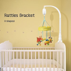 May include: A white baby crib with a mobile featuring plush toys in red, yellow, and blue. The mobile is suspended from a white bracket. Text on the wall reads "Rattles Bracket" and "H-shaped".