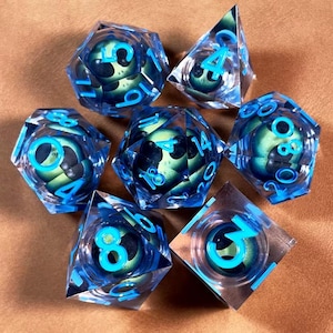 May include: A set of seven polyhedral dice with a fantasy theme. Each die is transparent blue with teal numbers and a green and black interior design. The dice are arranged on a brown surface.
