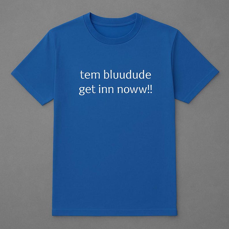 Puede incluir: Una camiseta azul real con el texto blanco "tem bluudude get inn noww!!" impreso en la parte delantera. La camiseta tiene mangas cortas y cuello redondo. El fondo es gris neutro.
