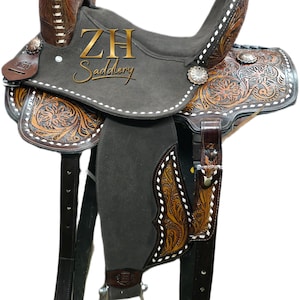 May include: A brown and grey Western saddle with detailed floral tooling and white stitching. The saddle features the text "ZH Saddlery". The stirrups and straps are dark brown.