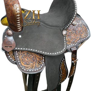 May include: A brown and black Western saddle with intricate floral tooling. The saddle features a dark gray seat, decorative silver conchos, and the text "ZH Saddlery". The saddle is designed for horseback riding.