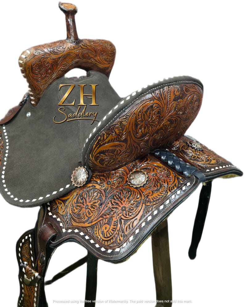 May include: A brown leather saddle with intricate floral carvings and white stitching. The saddle features a dark gray suede seat and silver-toned conchos. The text "ZH Saddlery" is visible on the saddle.