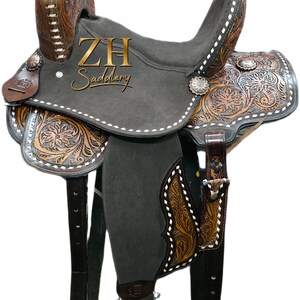 May include: A Western-style saddle with intricate floral and geometric tooling in shades of brown and tan. The saddle features a dark gray seat and the text "ZH Saddlery".