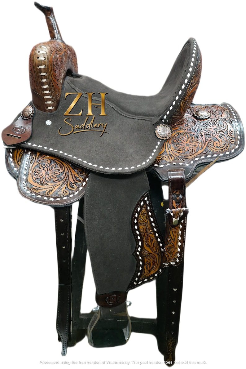 May include: A Western-style saddle with intricate floral and geometric tooling in shades of brown and tan. The saddle features a dark gray seat and the text "ZH Saddlery".