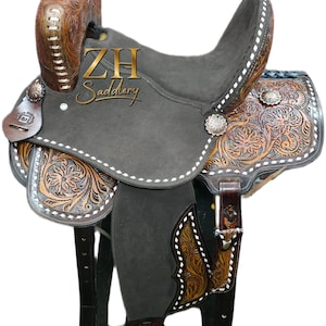 May include: A brown and gray Western saddle with intricate floral tooling. The saddle features a dark gray seat, decorative silver conchos, and the text "ZH Saddlery". The saddle is designed for horseback riding.