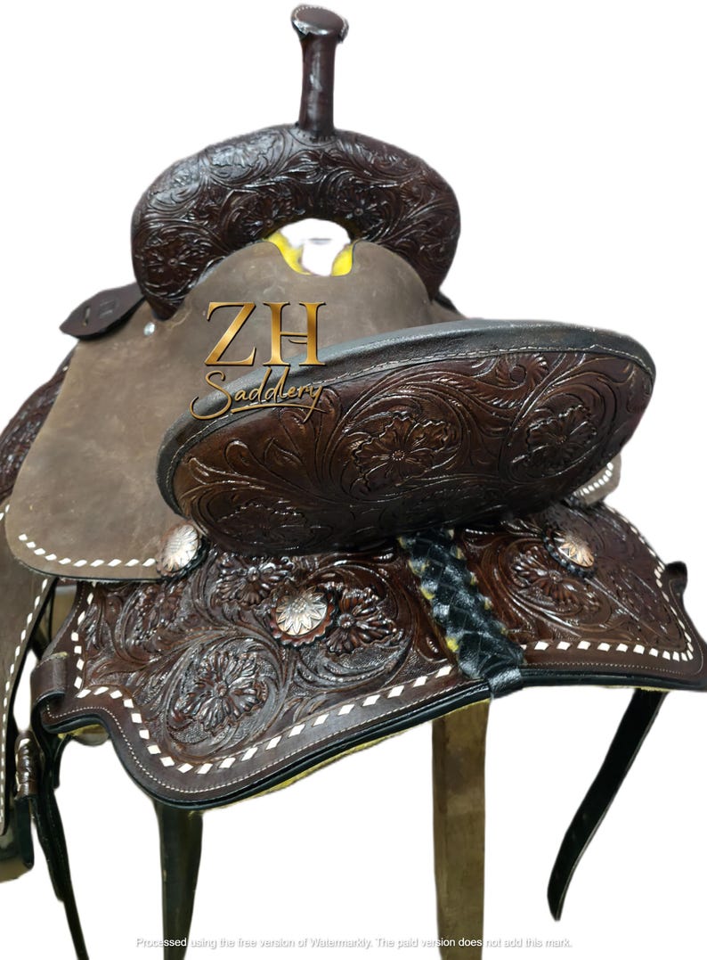 May include: A brown leather western saddle with intricate floral tooling and white stitching. The saddle features a high cantle, a horn, and stirrups. The text "ZH Saddlery" is visible on the saddle.