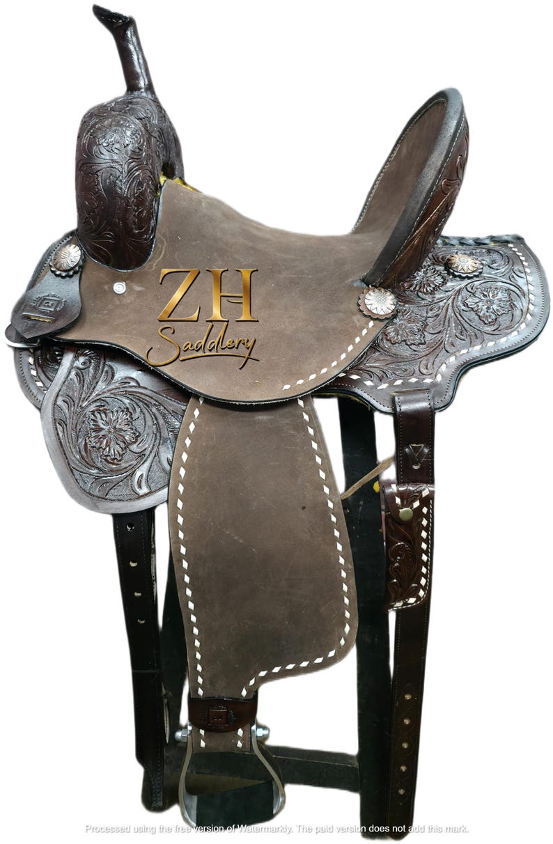 May include: A brown leather Western saddle with intricate floral tooling and silver accents. The saddle features a high cantle, a horn, and stirrups. The text "ZH Saddlery" is visible on the saddle. The saddle is designed for horseback riding.