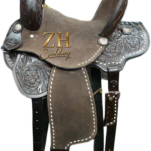 May include: A brown leather western saddle with intricate floral tooling and silver accents. The saddle features a high cantle, a horn, and stirrups. The text "ZH Saddlery" is visible on the saddle.