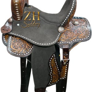 May include: A Western-style saddle with a gray suede seat and intricate floral tooling on the brown leather. The saddle features silver-toned conchos and white stitching. The text "ZH Saddlery" is visible on the saddle.