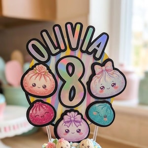 May include: A cake topper featuring the name OLIVIA and the number 8 in black, set against a pastel striped background with four cute, glittery, cartoon-style dumpling characters. The topper is displayed on a cupcake with blue frosting.