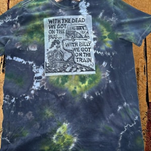 May include: A tie-dye t-shirt with a graphic print featuring a bus and a train, along with the text "WITH THE DEAD WE GOT ON THE BUS... WITH BILLY WE GOT ON THE TRAIN". The shirt has a blue, green, and white spiral pattern.