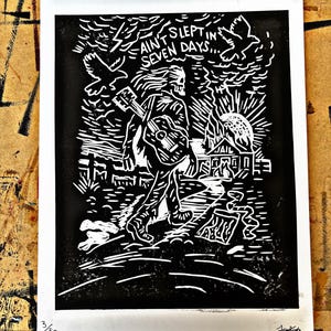Puede incluir: Grabado en linóleo en blanco y negro que representa una figura esquelética con una guitarra, caminando hacia una cárcel. El grabado incluye el texto "Ain't Slept in Seven Days..." y está numerado 3/50.