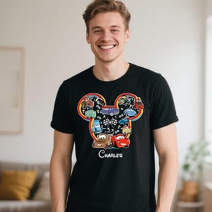 Puede incluir: Camiseta negra con un gr&aacute;fico colorido de coches de dibujos animados dispuestos en forma de cabeza de Mickey Mouse, con un arco&iacute;ris y banderas a cuadros. El nombre "Charles" est&aacute; impreso debajo.