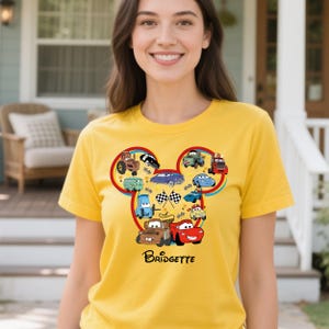 Puede incluir: Camiseta amarilla con un dise&ntilde;o de dibujos animados de coches en forma de cabeza de Mickey Mouse. El dise&ntilde;o incluye banderas de carreras y el nombre "Bridgette".
