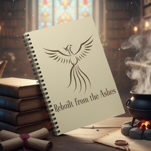 May include: A spiral-bound notebook with a phoenix illustration and the text "Rebuilt from the Ashes" sits on a wooden desk. Other items include a stack of books, a quill, a crystal ball, scrolls, and a cauldron with smoke, all in a library setting.